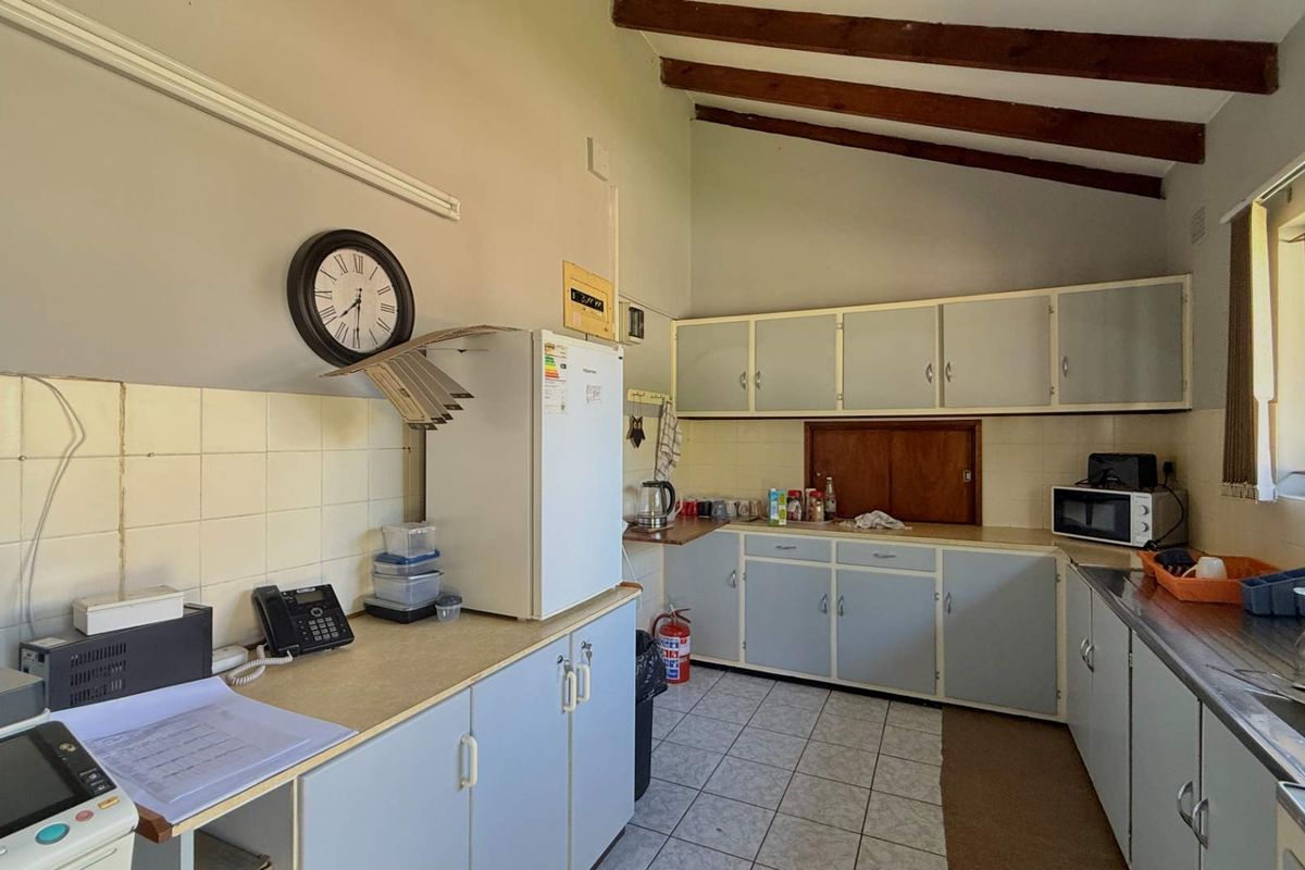 A functional kitchen featuring built-in cabinetry, laminate countertops, a stainless steel sink, and exposed timber ceiling beams, offering potential for modernization.