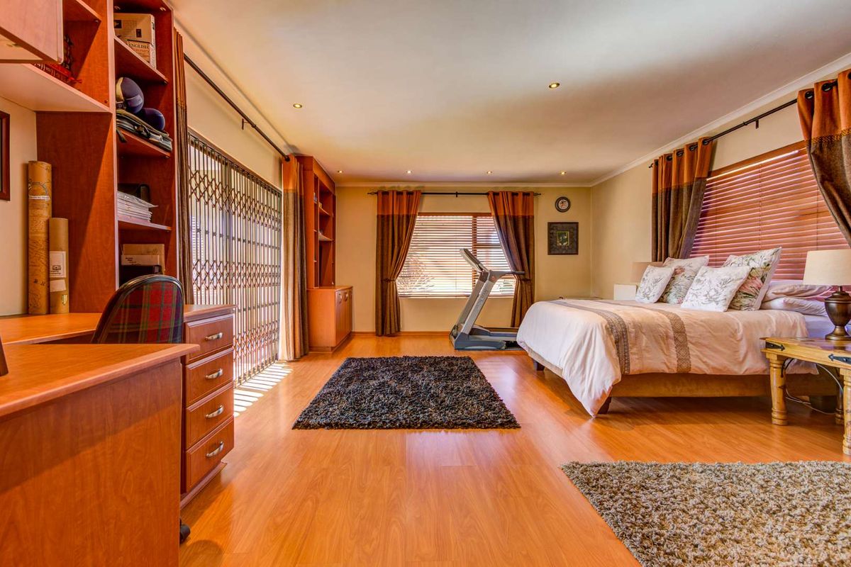Spacious bedroom featuring laminate flooring, built-in shelving units, recessed lighting, and large windows with venetian blinds and security gate access.