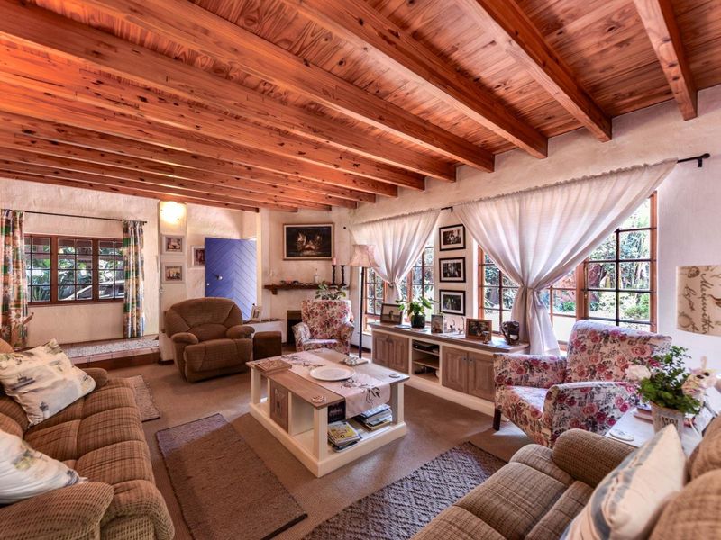Cozy living room featuring a rustic exposed timber beam ceiling, fireplace, and large timber-framed windows that provide natural light and garden views.