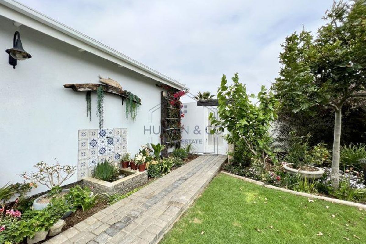 A well-maintained rear garden featuring a paved walkway, decorative tiled wall feature with integrated water element, and established landscaping.