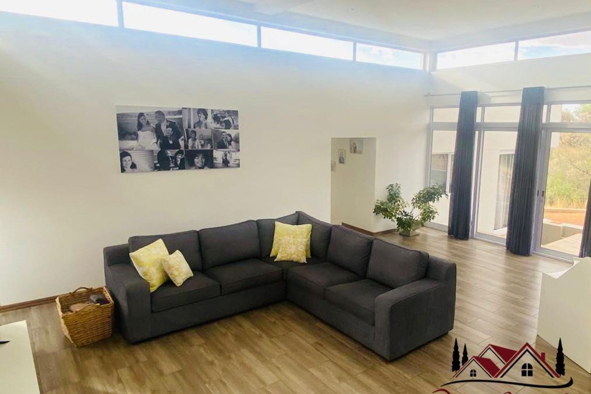 Spacious living area featuring high ceilings with clerestory windows, wood-look flooring, and large glass doors providing ample natural light and outdoor access.