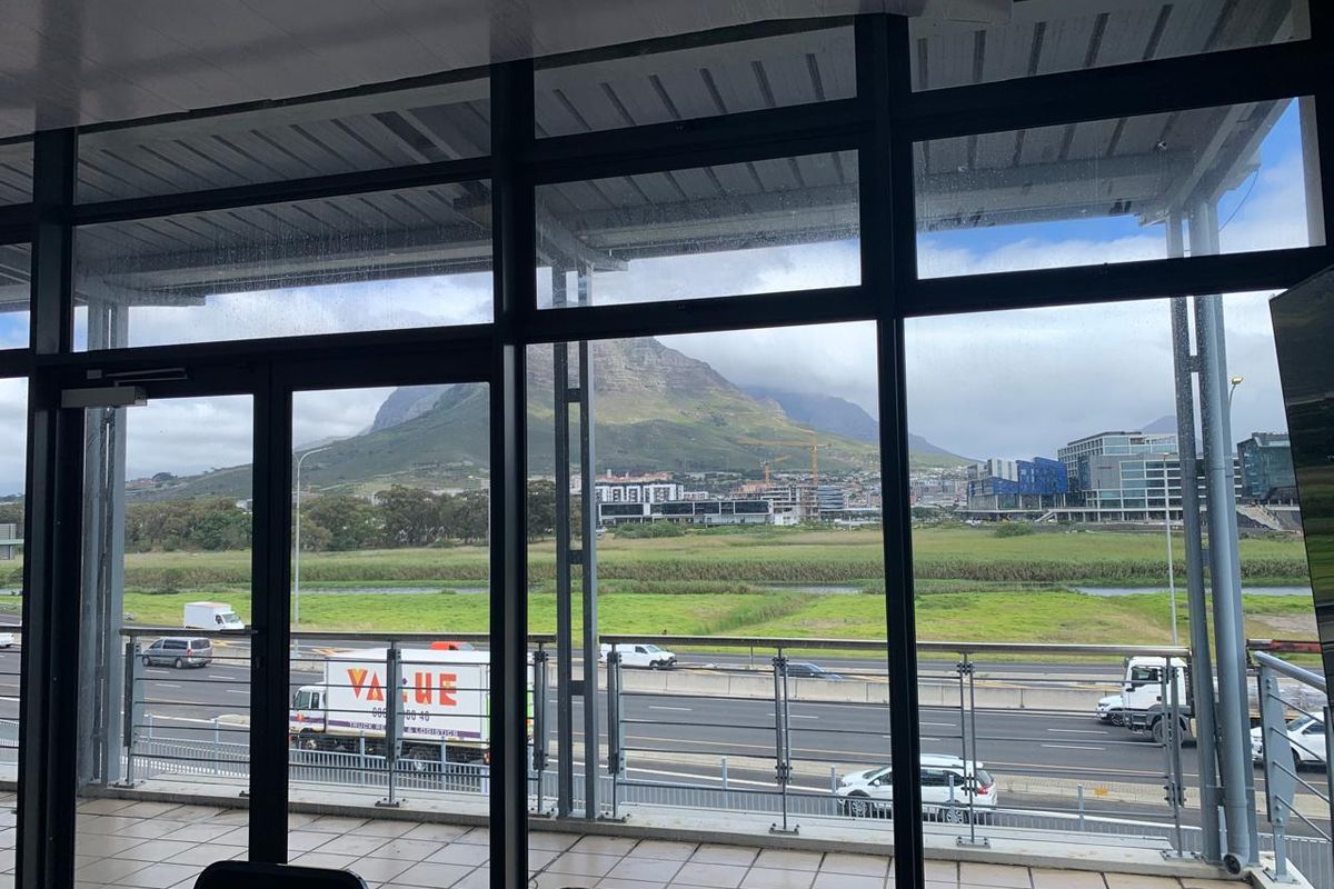 Modern office space featuring expansive floor-to-ceiling windows with panoramic mountain and highway views, leading out to a tiled balcony with a glass balustrade.