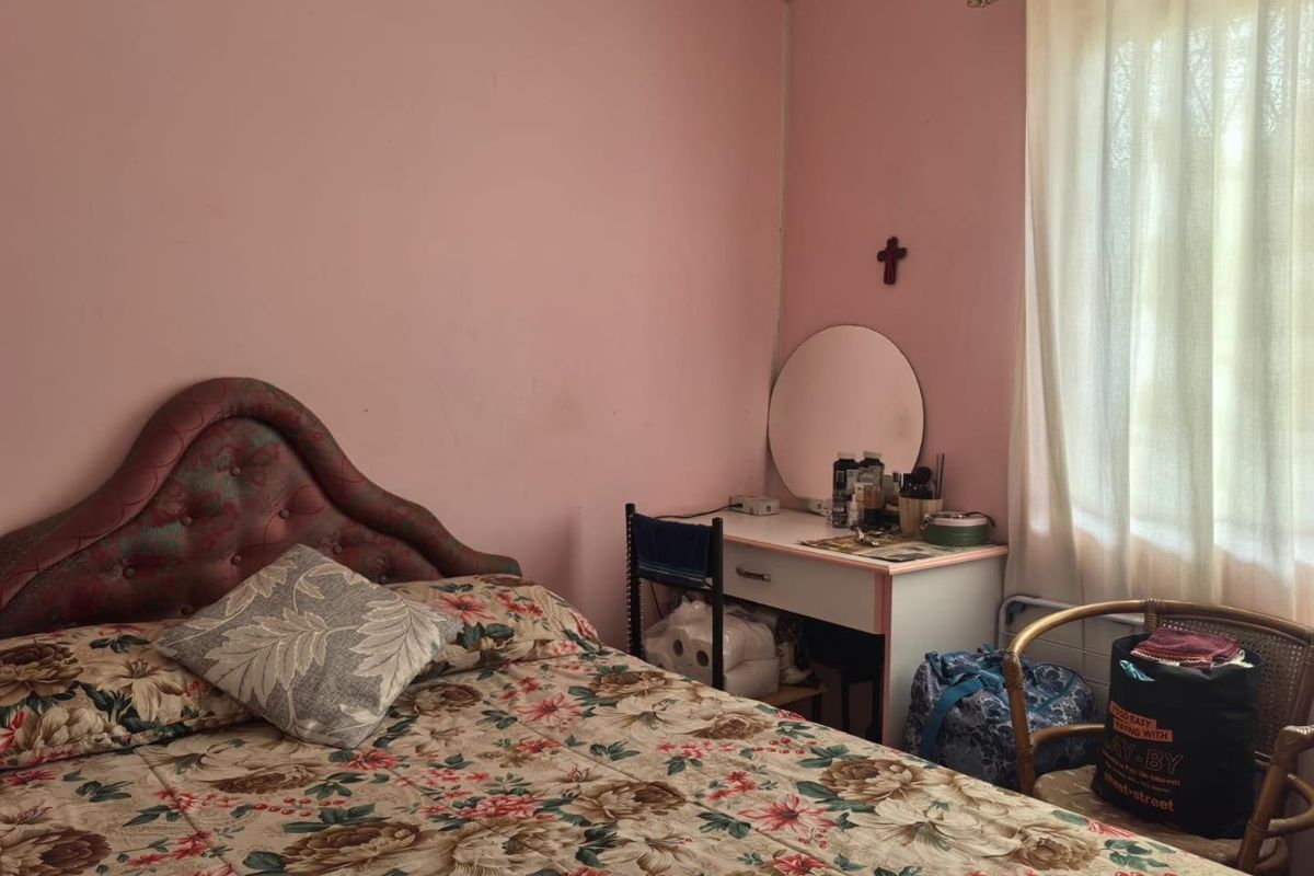 A bedroom featuring pink painted walls and a window with a curtain rod, offering a blank canvas for potential cosmetic updates.