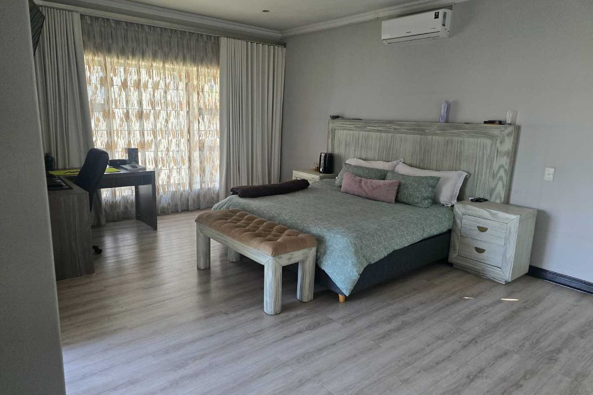 Spacious bedroom featuring light wood-look flooring, a wall-mounted air conditioning unit, and large windows with floor-to-ceiling curtains.