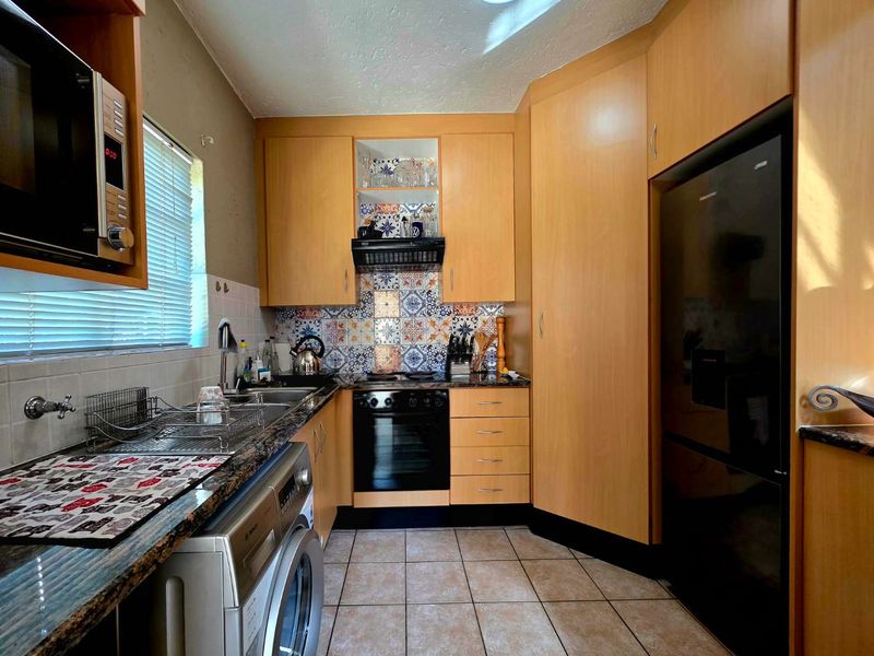 A functional kitchen featuring light wood cabinetry, patterned tile backsplash, granite-look countertops, and integrated appliances including an oven and extractor fan.