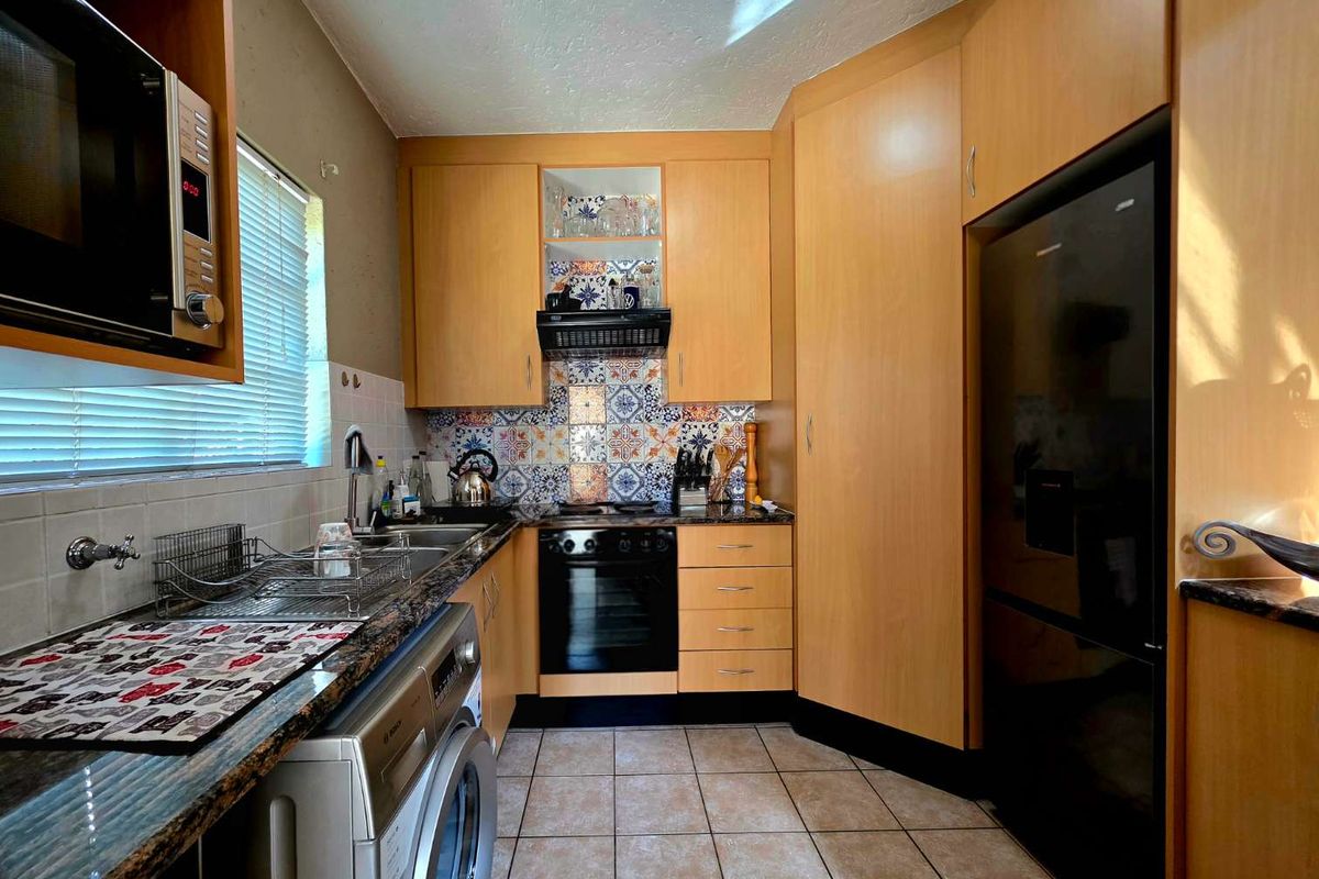 A functional kitchen featuring light wood cabinetry, patterned tile backsplash, granite-look countertops, and integrated appliances including an oven and extractor fan.