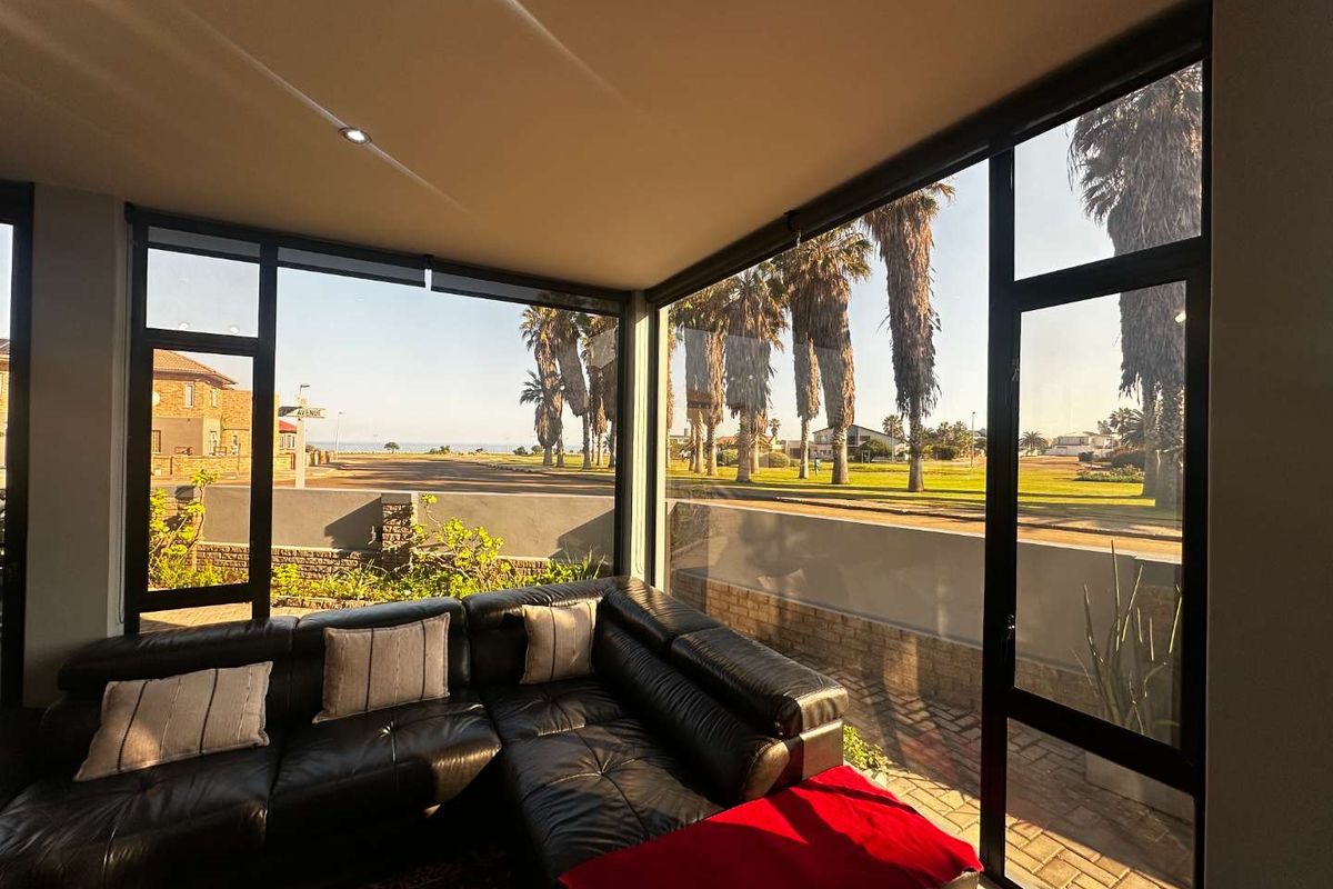 A bright living room featuring expansive floor-to-ceiling windows that offer panoramic views of the surrounding neighborhood and coastal landscape.