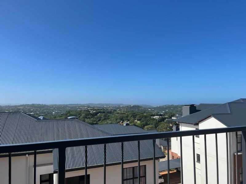 An elevated view from a balcony overlooking the surrounding residential neighborhood and lush green landscape under a clear blue sky.