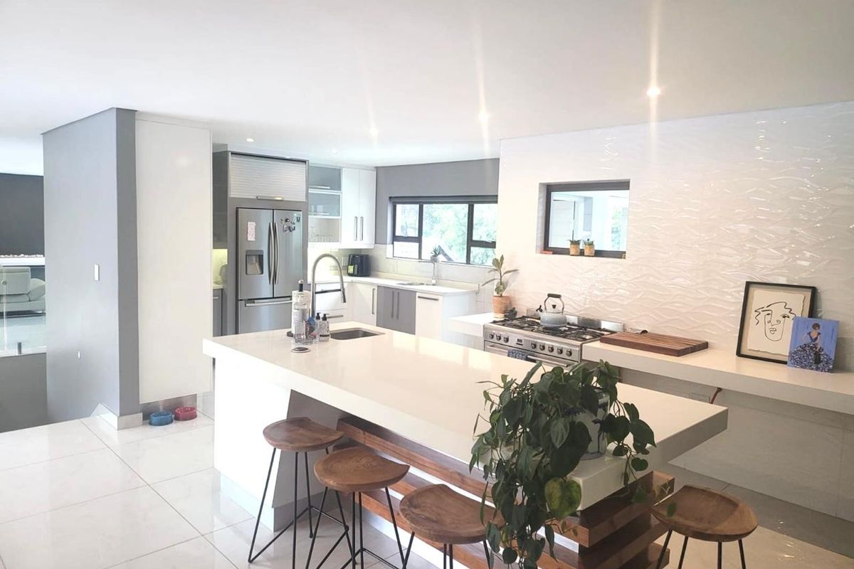 Modern open-plan kitchen featuring a large central island with quartz countertops, gas cooktop, integrated appliances, and sleek contemporary finishes throughout.