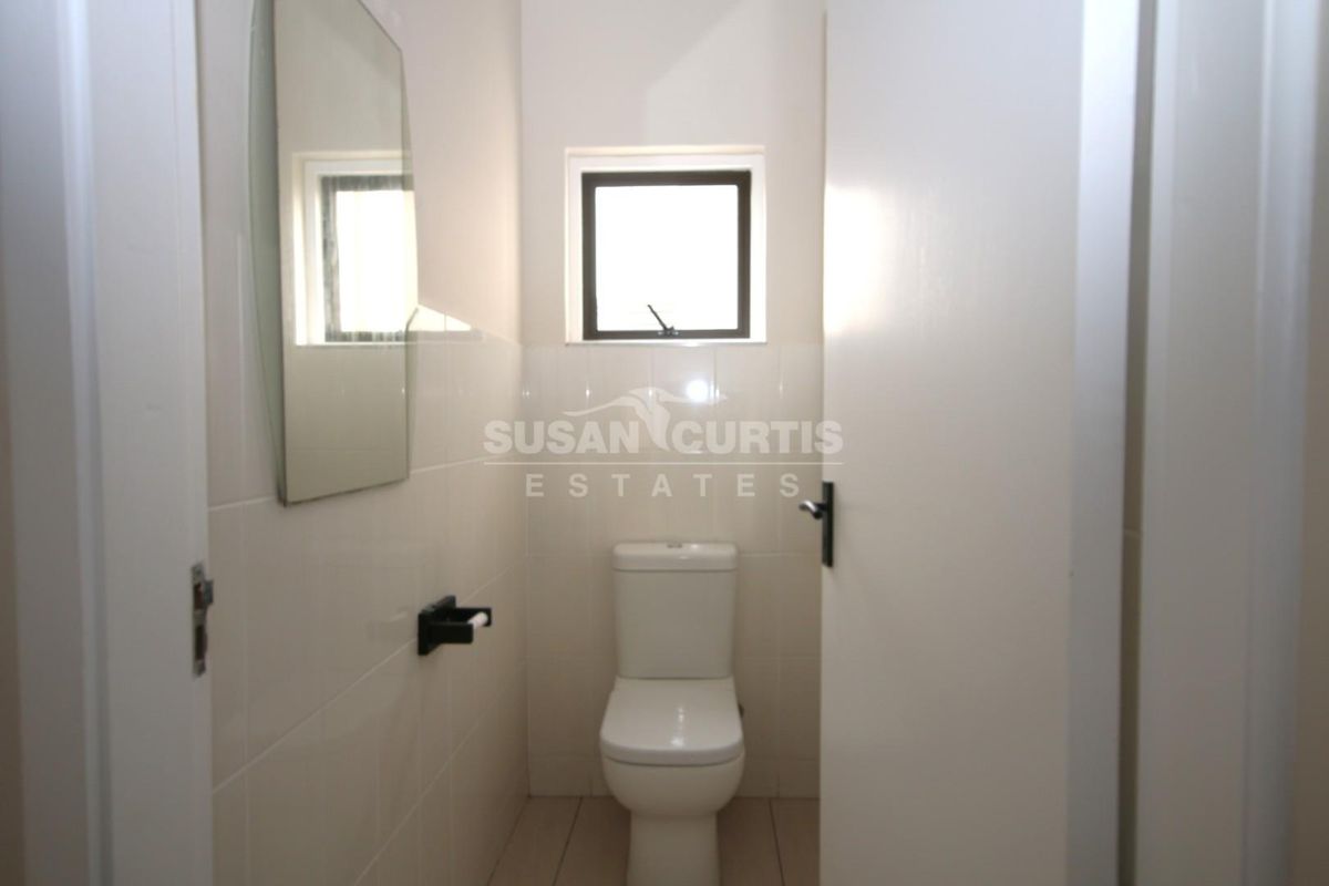A compact, neutral-toned guest bathroom featuring a standard toilet, tiled walls, and a wall-mounted mirror.