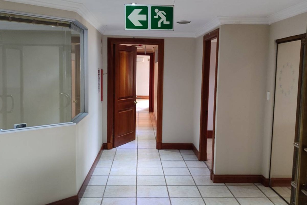 A clean office hallway featuring tiled flooring, glass partitioning, and wooden door frames, leading to multiple office spaces.