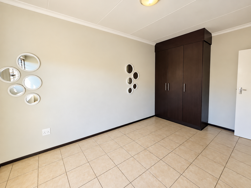 A clean, empty bedroom featuring neutral tiled flooring, a dark wood built-in wardrobe, and coved ceiling details.