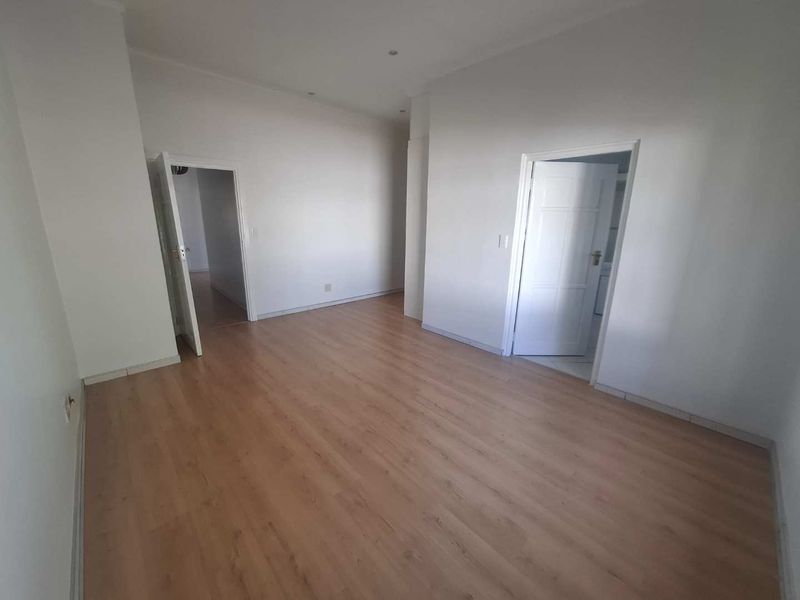 A bright, empty living room featuring light wood-look laminate flooring, neutral walls, and recessed downlighting, providing a clean and versatile blank canvas.