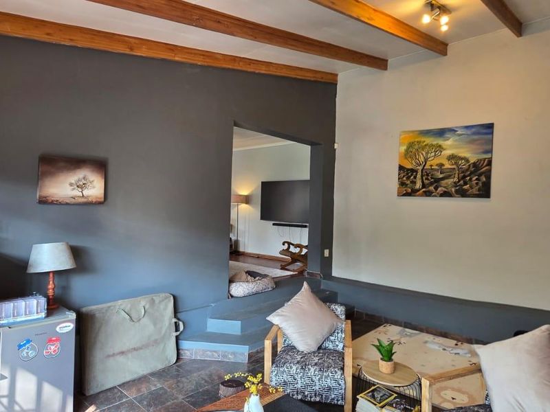 Living room featuring exposed timber ceiling beams, tiled flooring, and a raised transition area leading to an adjacent space.
