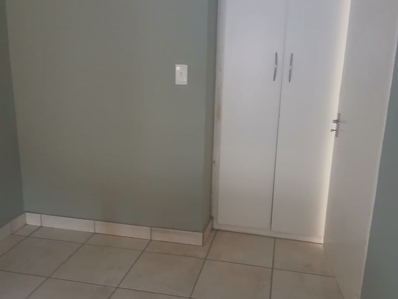 An empty bedroom featuring neutral wall paint, tiled flooring, and a built-in white cupboard.