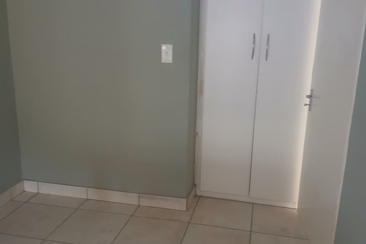 An empty bedroom featuring neutral wall paint, tiled flooring, and a built-in white cupboard.