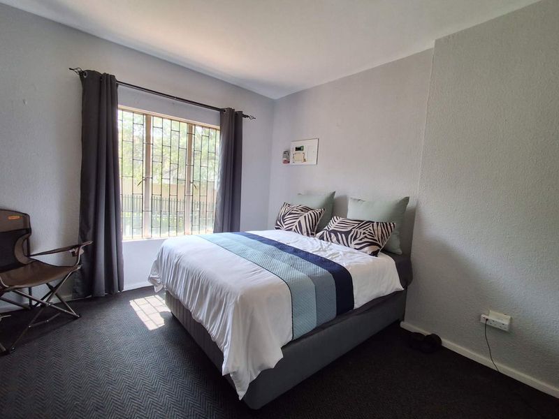 A functional bedroom featuring a window with security bars and neutral wall finishes, providing a comfortable space for rest.
