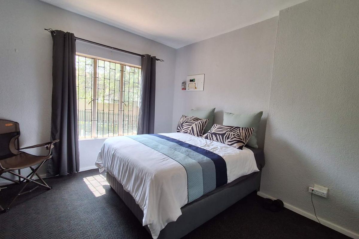 A functional bedroom featuring a window with security bars and neutral wall finishes, providing a comfortable space for rest.