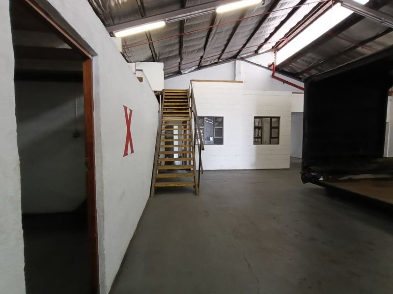 Spacious industrial utility area featuring concrete flooring, exposed roof trusses, and a timber staircase leading to an upper level.