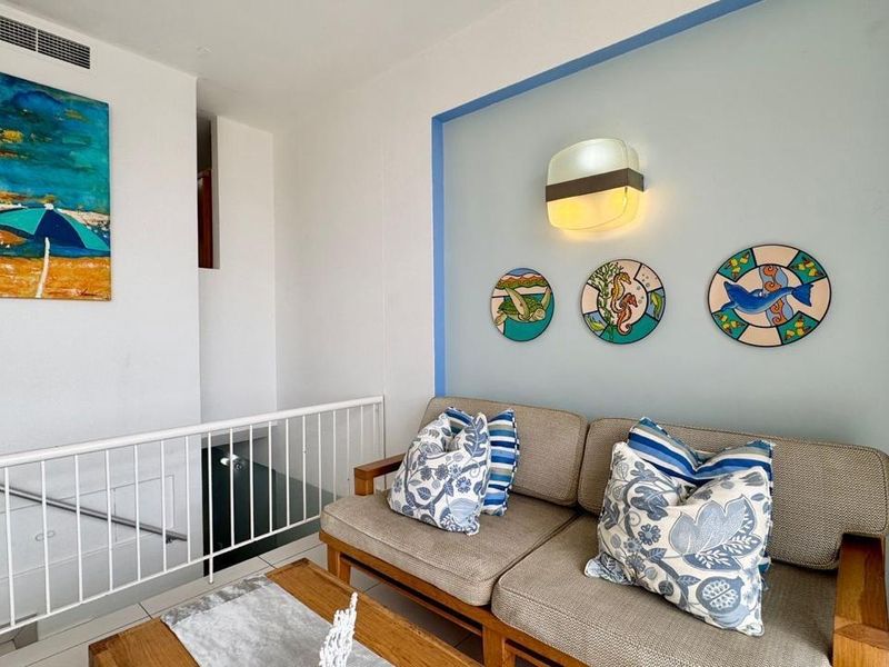 A bright living area featuring a staircase with a white metal railing, a feature wall with accent lighting, and neutral tiled flooring.