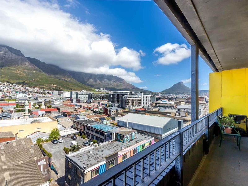 A spacious balcony featuring a metal balustrade and yellow wall cladding, offering expansive panoramic views of the city and surrounding mountains.