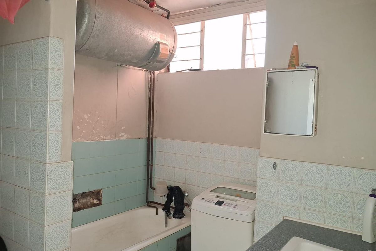 A dated bathroom featuring a bathtub, basin, and exposed electric water heater, requiring significant renovation and cosmetic updates to improve functionality and aesthetics.