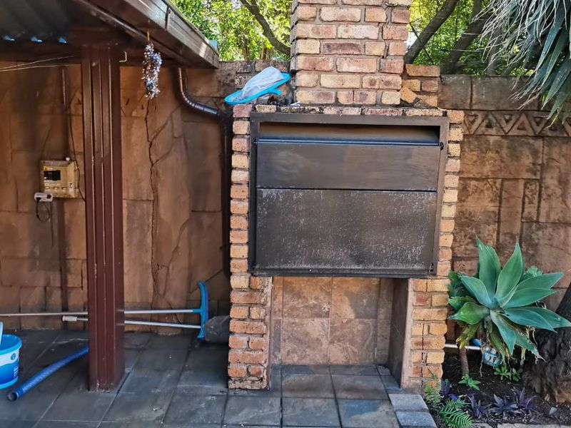Outdoor covered patio area featuring a built-in brick braai, tiled flooring, and decorative stone-cladding wall finish.