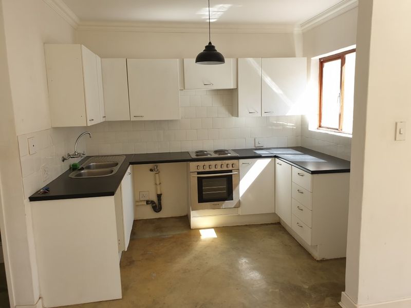 A functional kitchen featuring white cabinetry, dark countertops, and a built-in oven, currently awaiting flooring and minor finishing touches.