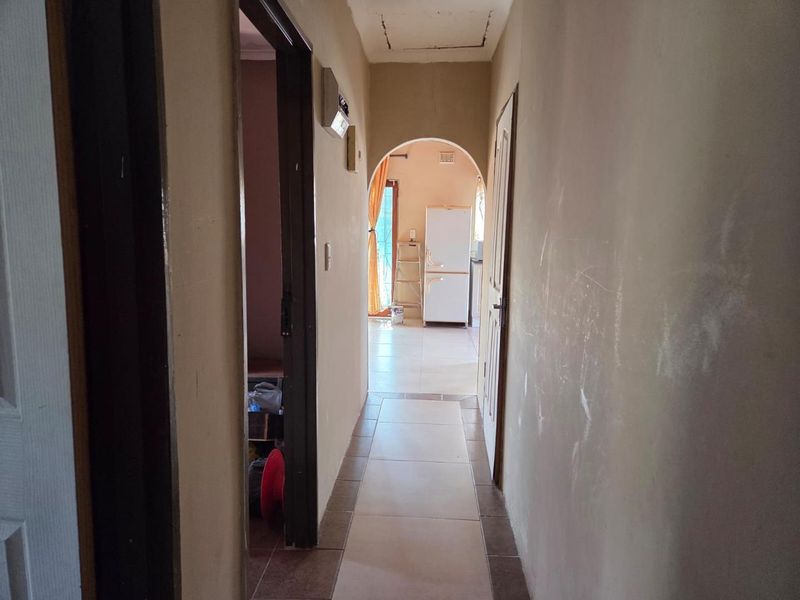 A narrow interior hallway featuring tiled flooring and an arched transition leading to an adjacent room, showing signs of wear on the walls.