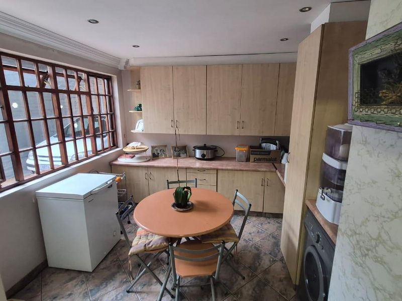 A functional kitchen featuring laminate cabinetry, tiled flooring, and a large timber-framed window providing natural light.