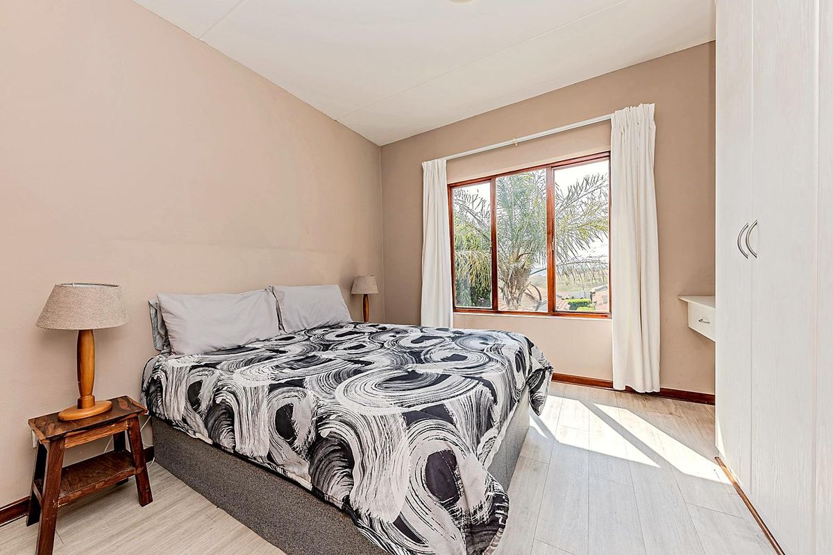 A bright bedroom featuring light-toned wood-look flooring, built-in wardrobe storage, and a large window providing natural light and exterior views.