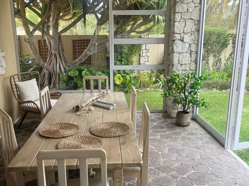 A bright, enclosed patio featuring flagstone flooring, stone-clad pillars, and expansive glass walls overlooking a lush garden.