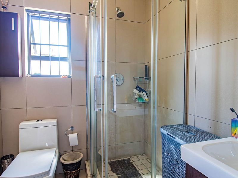 A functional bathroom featuring a glass shower enclosure, a modern toilet, and a vanity basin with tiled wall finishes.
