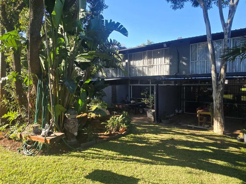 Rear view of the townhouse featuring a covered patio area, established garden, and large sliding doors providing access to the interior.