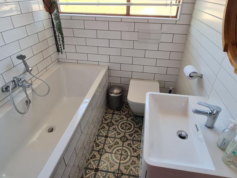 A modern bathroom featuring a bathtub with shower mixer, wall-hung toilet, vanity basin, and stylish subway wall tiles with patterned floor tiling.
