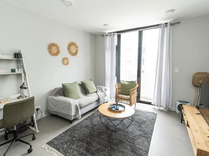 A bright and modern living room featuring tiled flooring, neutral walls, and a large sliding glass door providing access to the balcony.