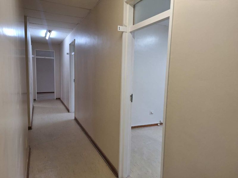 A functional office hallway featuring tiled flooring, fluorescent lighting, and multiple internal access doors leading to individual office spaces.