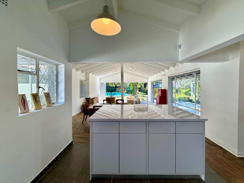 Spacious open-plan living area featuring a modern kitchen island, vaulted ceilings with exposed beams, and seamless flow to the outdoor pool area.
