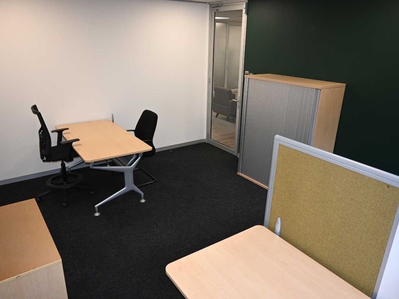 A functional office space featuring carpeted flooring, a glass entry door, and a partition wall, providing a professional work environment.