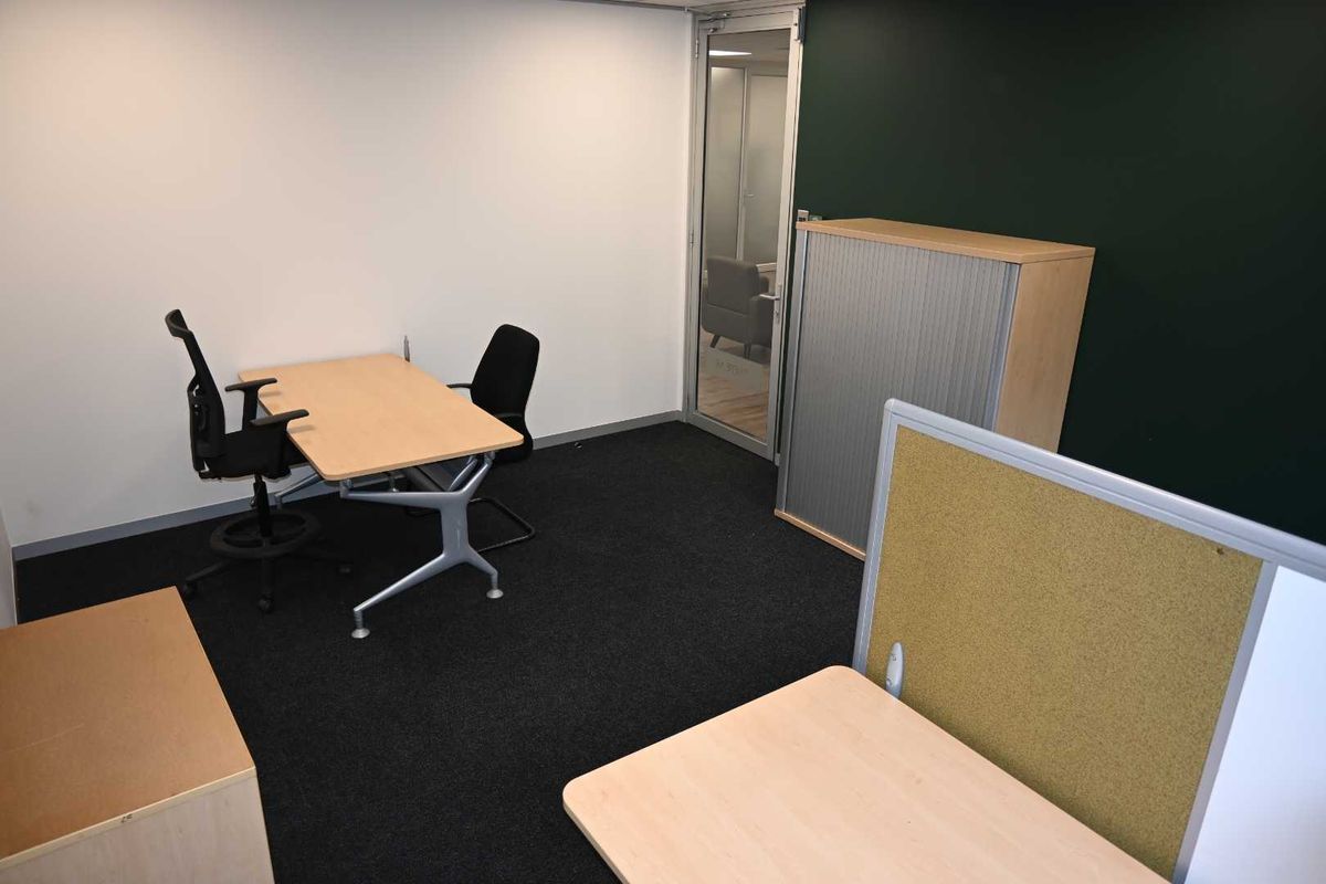 A functional office space featuring carpeted flooring, a glass entry door, and a partition wall, providing a professional work environment.