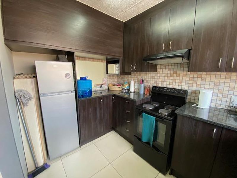 A functional kitchen featuring dark wood cabinetry, granite countertops, a mosaic tile backsplash, and a built-in electric stove with an extractor fan.