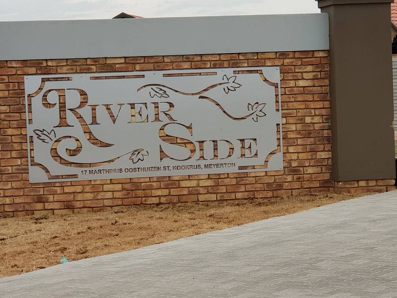 A clear view of the Riverside complex entrance signage mounted on a brick boundary wall with paved driveway access.