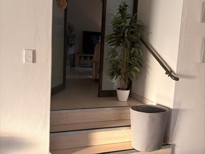 An interior entry area featuring timber-look laminate stairs with metal nosing, a handrail, and a sliding glass door leading to the living space.