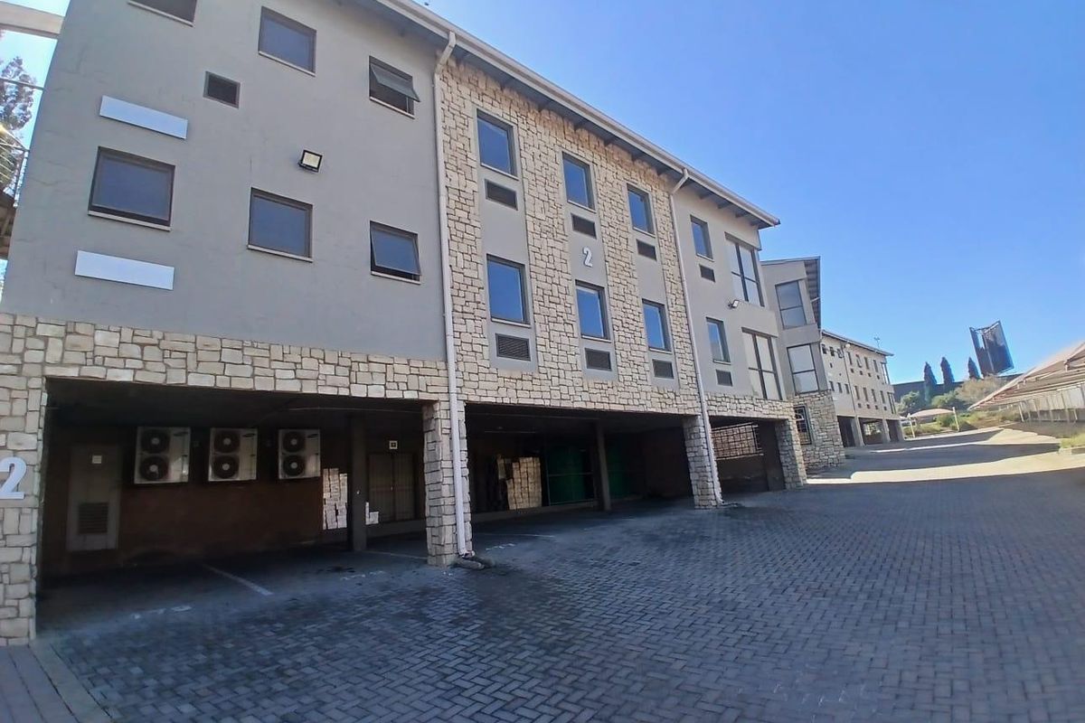 Exterior view of a multi-story commercial building featuring stone cladding, paved parking area, and mounted air conditioning units.