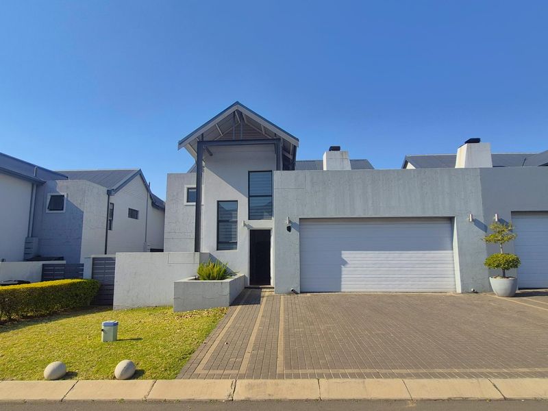 Front elevation of a modern cluster home featuring a paved driveway, double garage, and contemporary architectural design with a pitched roof.