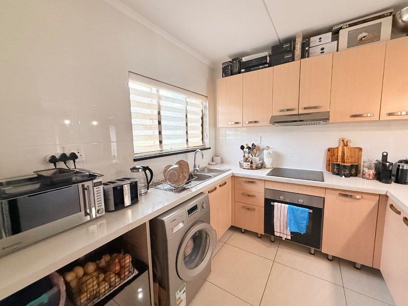 A functional kitchen featuring light wood-finish cabinetry, integrated appliances including an oven and hob, tiled backsplash, and tiled flooring.