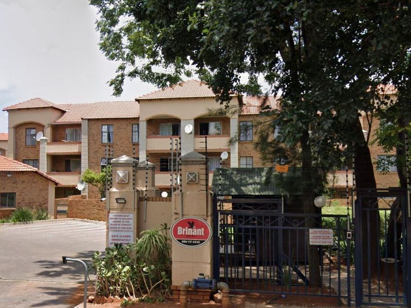 Front view of a multi-story apartment complex featuring brick construction, tiled roofing, and secure gated access with electric fencing.
