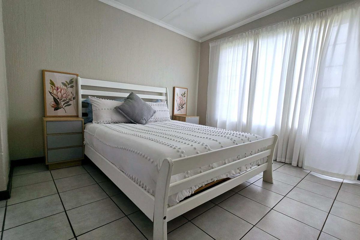 A well-lit bedroom featuring neutral wall finishes, tiled flooring, and large windows with curtains, providing a comfortable and functional living space.