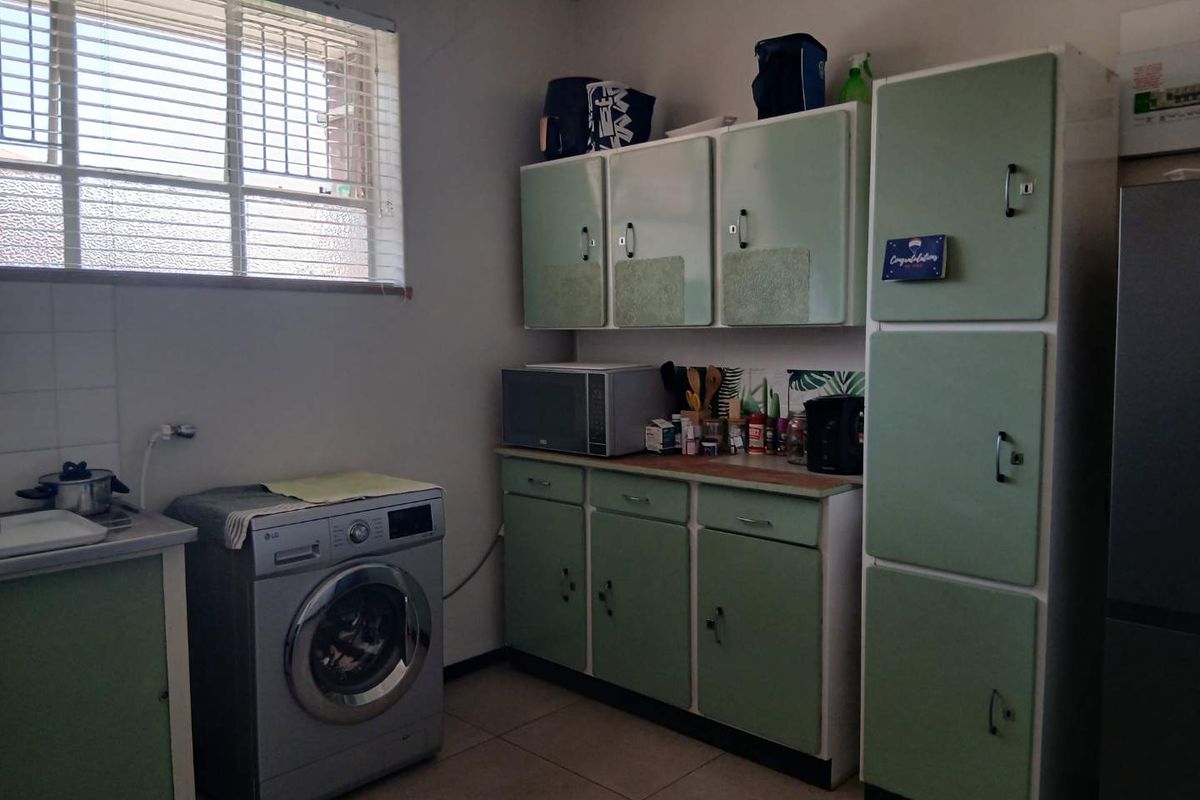 A functional kitchen area featuring vintage-style built-in cabinetry, tiled flooring, and dedicated plumbing connections for laundry appliances.