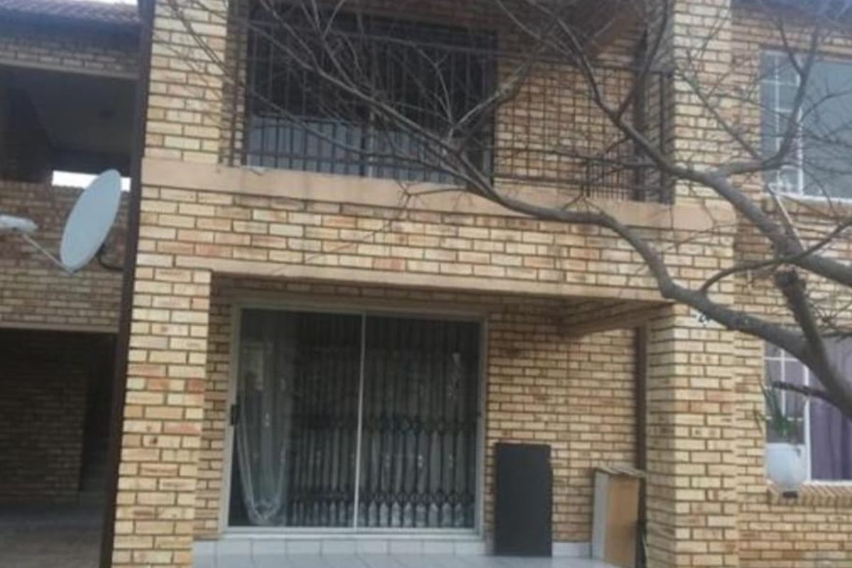Rear view of a two-story face brick apartment building featuring a ground-floor tiled patio with sliding doors and an upper-level balcony.